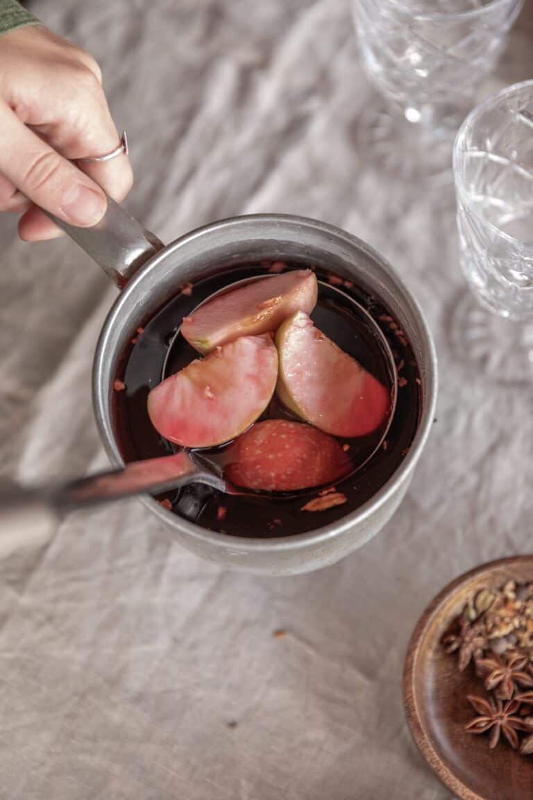 Eine Frau erhitzt vorsichtig einen Glühwein mit Gewürzen und frischen Äpfeln.