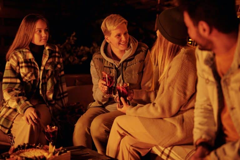 Eine Gruppe Glühwein Freunde wärmt sich mit einer Tasse Glühwein an einem Kalten Winterabend auf.